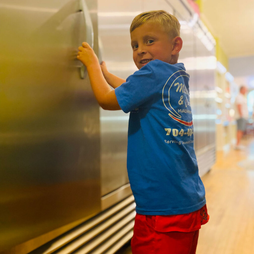 boy opening freezer, wearing Miller and Condrey HVAC and Refrigeration t-shirt
