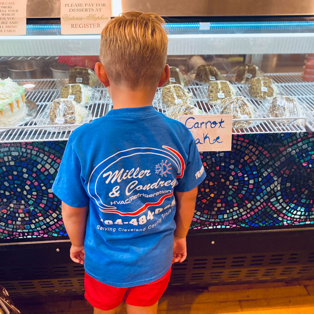 boy standing in front of cake in refrigerated display wearing a Miller and Condrey shirt